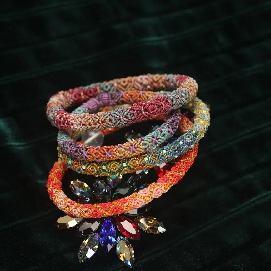 Stack of jewel-accented woven bracelets in rainbow gradient on dark velvet