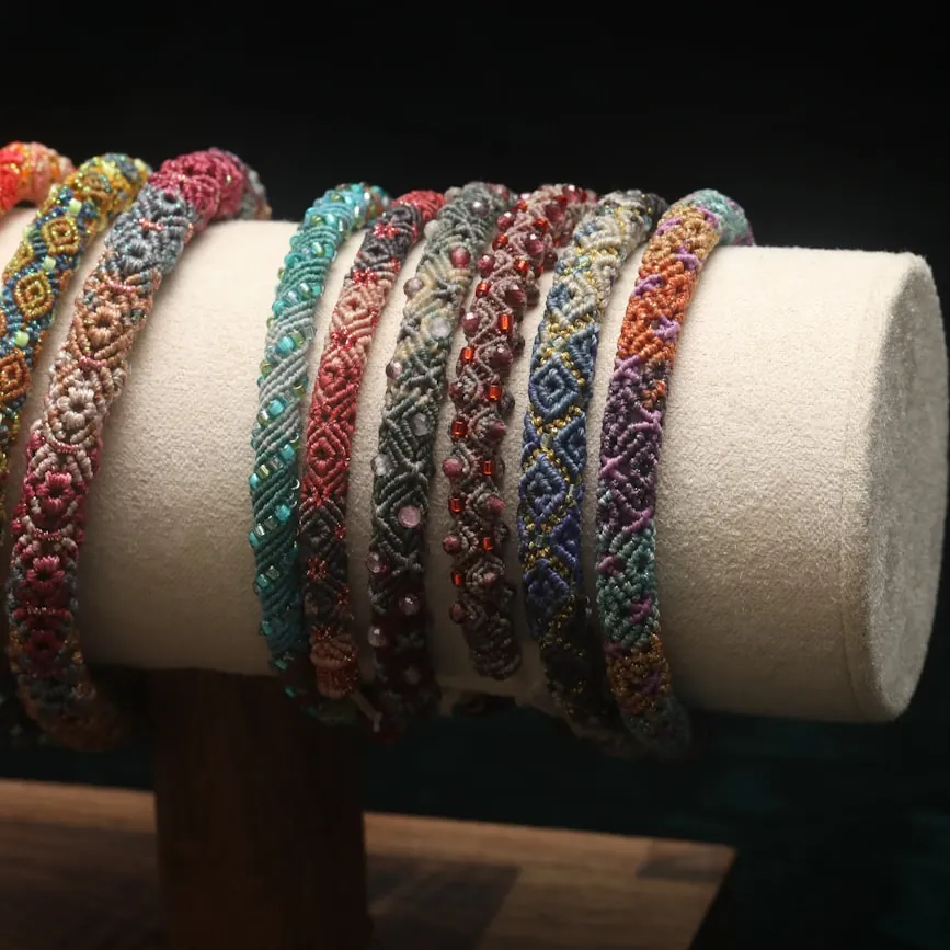 Row of woven and beaded bracelets in rainbow colors displayed on a cream stand