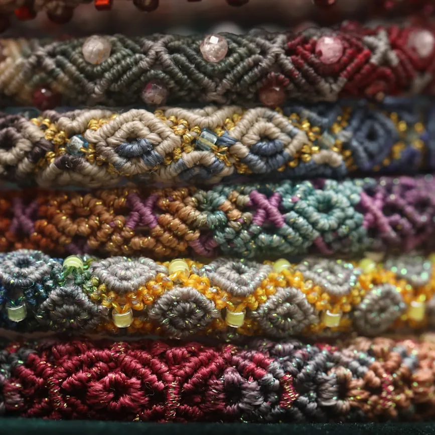 Close-up of finely woven friendship bracelets stacked in jewel-tone rainbow rows